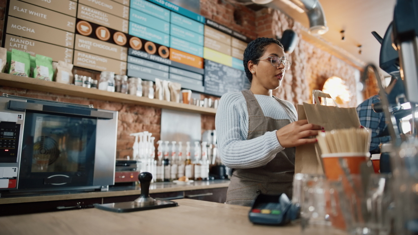 Friendly Latin Barista Serves Order to a Food Delivery Courier Picking Up Two Take Away Coffees and Pastries from a Cafe Restaurant. Delivery Guy Puts Food in His Hot Thermal Insulated Bag. | Shutterstock HD Video #1062664426