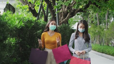 Asian woman wearing face mask. Happy woman with shopping bags enjoying in shopping. Girl holding colour paper bag.Friends walking in shopping mall.time shopping coronavirus crisis or covid19 outbreak.