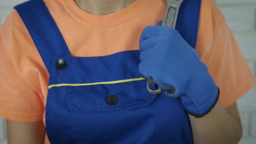 Holds construction tools. A good-looking woman in inuform with a spanner look in the camera in the room.