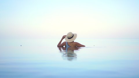 Lonely Female With Hat in Infinity Pool Looking at Skyline. Heavenly Dream Scene Lavish Lifestyle Concept, Slow Motion