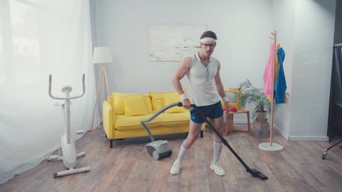 Energetic sportsman wagging hips, while vacuum cleaning living room