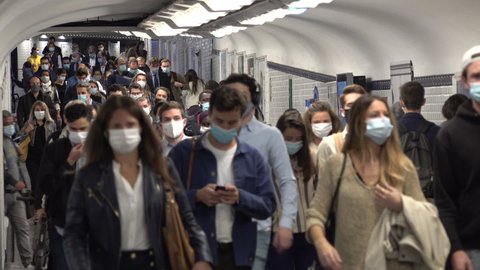 PARIS, FRANCE – SEPTEMBER 2020: Covid-19 coronavirus global pandemic. Commuting railway passengers wearing protective face masks walk through busy corridor in metro system of Paris, public transport 