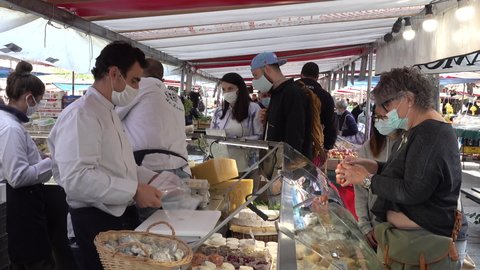 PARIS, FRANCE – SEPTEMBER 2020: Covid-19 coronavirus pandemic in daily life, people wear mandatory face masks at outdoor food market. Vendors selling cheese at specialized store in Paris, France