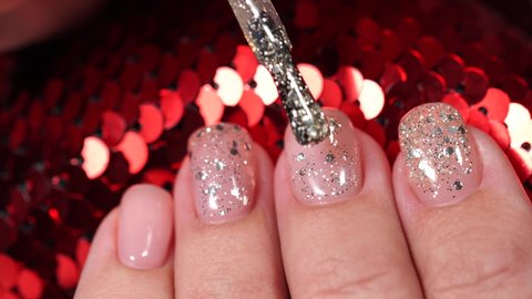 Woman applying modern trendy shiny sparkling silver gel polish to painted with tender pastel pink color nails. Closeup view 4k video of painted fingernails isolated on red shiny Christmas background