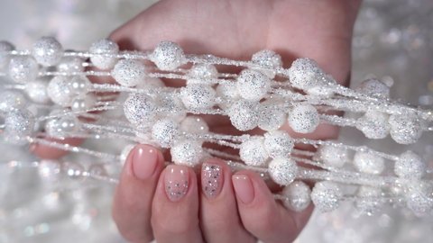 Closeup top view 4k video of female hands with professional pink manicure with glittering silver sparkles isolated. Modern festive minimal gel polish nail design. Woman holding white Christmas picks