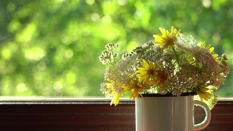 Woman decorates her home with cute field flowers. Bunch of wild plants in blue metal mug standing on windowsill.