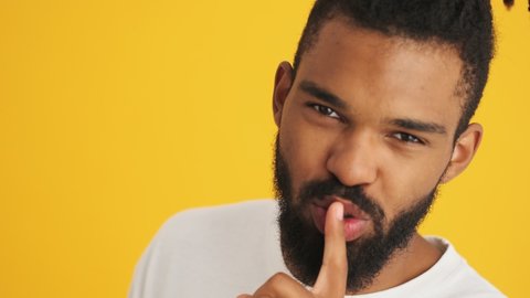 Young handsome positive african man showing silence gesture and winking isolated over yellow background