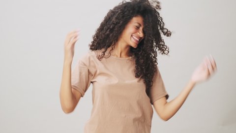 A happy african american woman is shaking her hair standing isolated over beige background