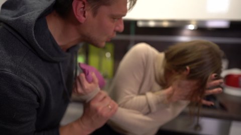 Male aggressor and his victim in the kitchen. The husband beats his wife, the woman covers her face with her hands. Abuse and Domestic Violence Concept