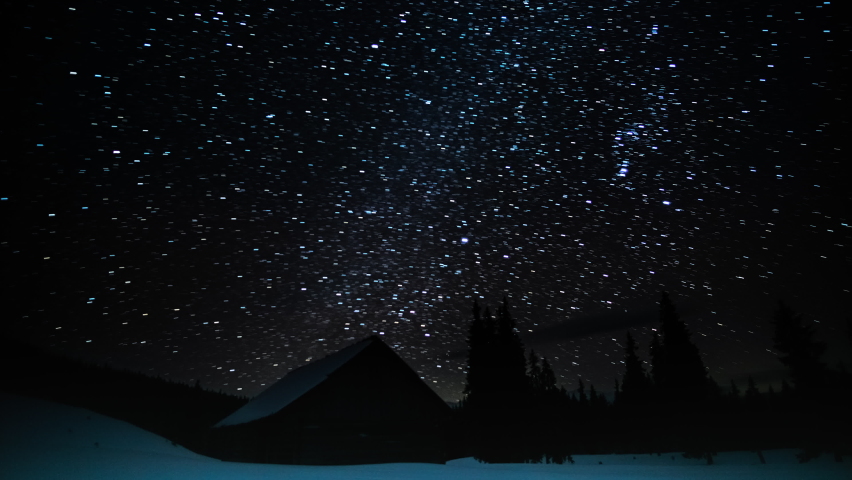 Wooden house in the mountains in winter. Stars move around a polar star. Time lapse of Star trails in the night sky. 4K