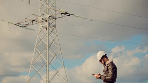 Engineer In Hardhat Maintenance Electricity Transmission Pylon.Technician Checking High Voltage Sensor Power Line Wires. Electrical Engineer In Helmet Power Lines.Technician Inspect High Voltage Tower