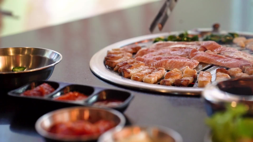 A customer grabbing grilled pork from a grill in a Korean style grilled pork restaurant