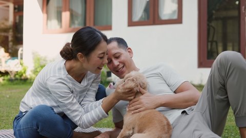 Cheerful young Asian family couple smiling bonding with his dog in the house. They give their little dog some love through a hug. Couples tease each other