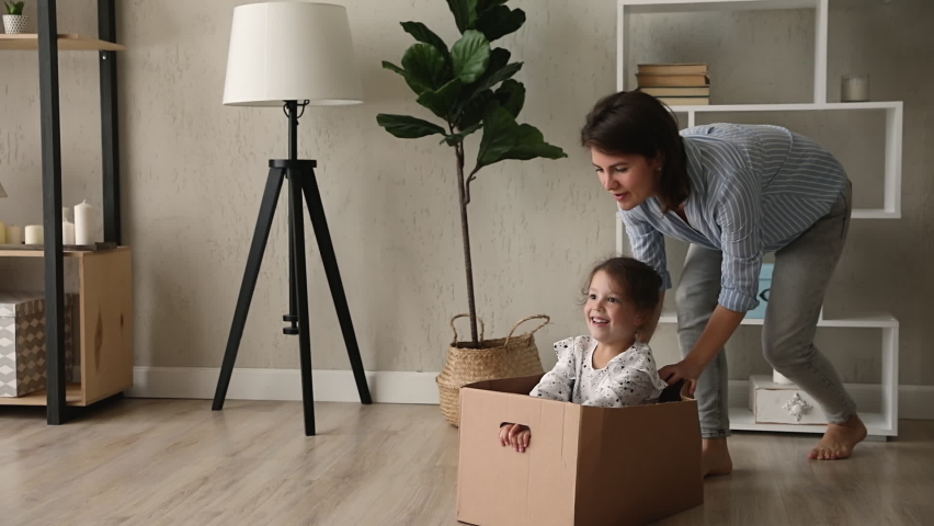 Young mom and small daughter play crazy creative games at home, mother barefoot run ride cute kid girl while she sit inside of big carton box, family fool around enjoy playtime at new modern warm flat | Shutterstock HD Video #1062680134