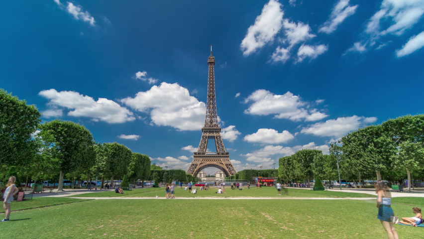 Eiffel Tower on Champs de Mars in Paris timelapse hyperlapse, France. Blue cloudy sky at summer day with green lawn and people walking around