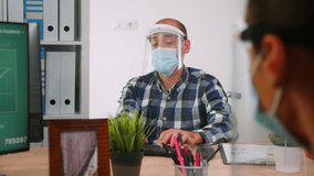 Handicapped businessman with visor and protection mask discussing with colleague working in new normal business office. Man respecting social distance in financial company during global pandemic. - Powered by Shutterstock - Get 15% off with code: PIKWIZARD15