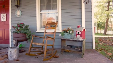 Clifton, VA, USA 11/14/2020: A 19th century historic house with vintage porch decoration featuring a wooden rocking chair, potted flowers, a metal pitcher and fallen autumn leaves and other ornaments.