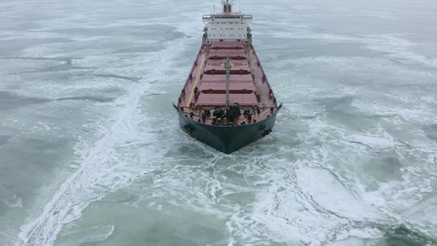 Aerial above epic huge steel ship breaks ice by bow of ship and floats in large sea ice floes. Maintaining navigation in a frozen sea channel laying. Self-propelled specialized vessel red ship.