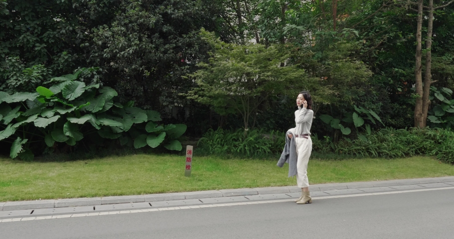 Side view of pretty young asian woman talking on the phone walking on the road with plant by the side beautiful young Chinese woman lifestyles 4k footage