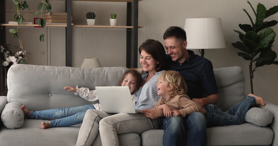 Relaxed couple their preschool son and daughter rest on comfy sofa in living room spend weekend laughing watching family movie or cartoons on laptop, enjoy free time at home, modern tech usage concept Royalty-Free Stock Footage #1062694759