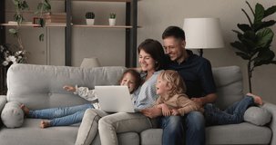 Relaxed couple their preschool son and daughter rest on comfy sofa in living room spend weekend laughing watching family movie or cartoons on laptop, enjoy free time at home, modern tech usage concept