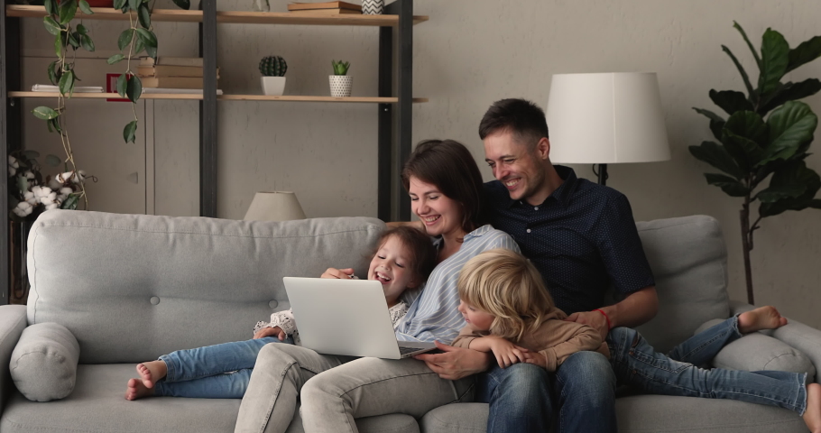 Relaxed couple their preschool son and daughter rest on comfy sofa in living room spend weekend laughing watching family movie or cartoons on laptop, enjoy free time at home, modern tech usage concept Royalty-Free Stock Footage #1062694759