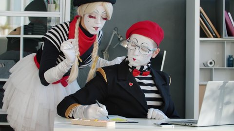 Mime businessman is using laptop typing while girl secretary is bringing document to sign in office. Corporate activities and pantomime concept.