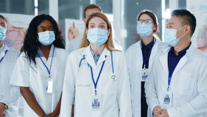 Multi-race diverse young medical staff communicating meeting in office workspace applauding hearing news watching TV celebrating ending of quarantine in masks. Royalty-Free Stock Footage #1062708409