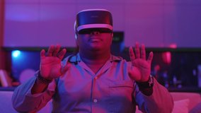 Smiling mixed race young man wearing virtual reality headset sitting on sofa at home neon light. Fun game. VR glasses Social network robot. Slow motion - Powered by Shutterstock - Get 15% off with code: PIKWIZARD15