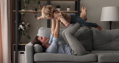 Loving young mom lying on couch play with preschool son imitate plane fly in air, happy mother relax have fun with little boy, enjoy family active weekend together at home, games and leisure concept