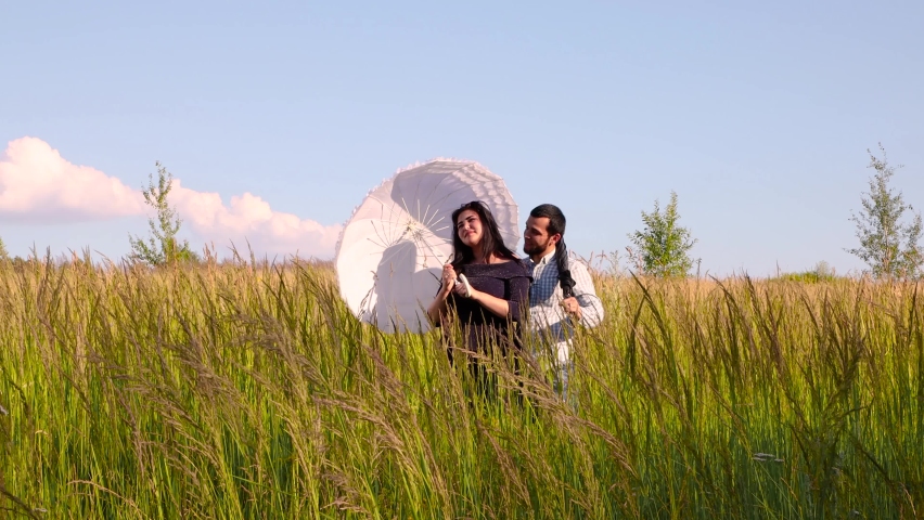 A girl and a man stand in a field under a white umbrella. Against the background of the blue sky. Warm summer day.