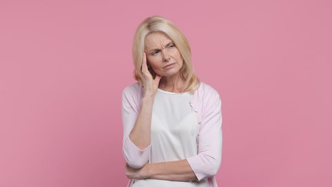 Thoughtful pensive elderly gray-haired blonde woman lady 40s 50s years old in white blank casual t-shirt prop up chin with hand think about something important isolated on pastel pink color background