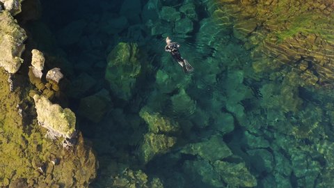 Aerial: Snorkeler swimming in Silfra popular diving / snorkeling fissure in Iceland between Eurasian and North American tectonic plates Thingvellir national park Phenomenal water clarity