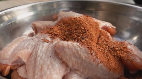 A mix of spices and salt is falling on the raw chicken wings in the bowl in slow motion