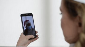 A young girl in a medical mask, in a New Year's Santa Claus hat, talks on video communication with her friend
