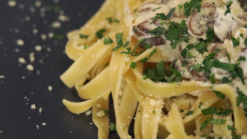 Close up of pasta with mushrooms, cream sauce and Parmesan cheese rotates on plate and twirl pasta on fork. Cooking fettuccine pasta. Italian Cuisine. Food background Royalty-Free Stock Footage #1062722566