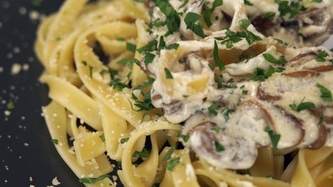 Close up of pasta with mushrooms, cream sauce and Parmesan cheese rotates on plate and twirl pasta on fork. Cooking fettuccine pasta. Italian Cuisine. Food background