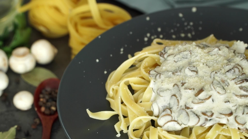 Pasta with mushrooms, cheese and cream sauce rotates on plate, and is sprinkled with parsley. Cooking fettuccine pasta. Italian Cuisine. Food background