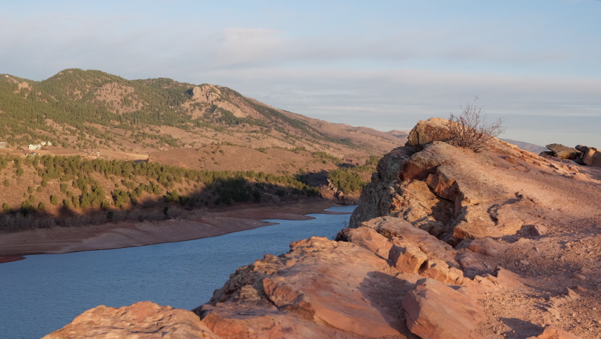 male hiker with a backpack and trekking poles on a cliff overlooking Horsetooth Reservoir, popular recreation destination in northern Colorado, fall scenery at sunrise