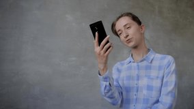 Positive woman in plaid shirt using smartphone, having video chat, job interview or distant consultation in room with grey wall - slow motion. Communication, conference, online technology concept
