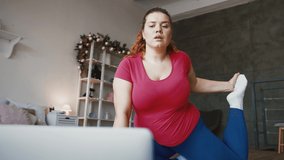 Online fitness training. Below shot of young plus size lady training stretching exercises, watching lesson on laptop and repeating it