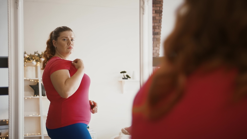 Body weight problem. Depressed lady with excess weight looking at mirror, feeling stressed about her figure and obesity Royalty-Free Stock Footage #1062728413