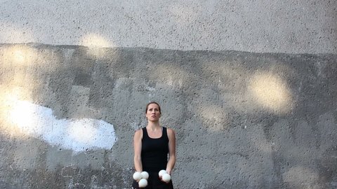 A professional juggler juggles with white balls. An attractive female juggler trains her juggling skills. A professional circus actress juggles with white balls on the street.