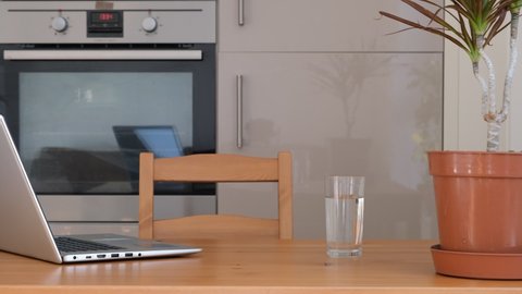 Home office. Work from home. Working place at home kitchen. Wooden table with laptop, plant and glass of water. Beige natural colors. Modern flat interior. 