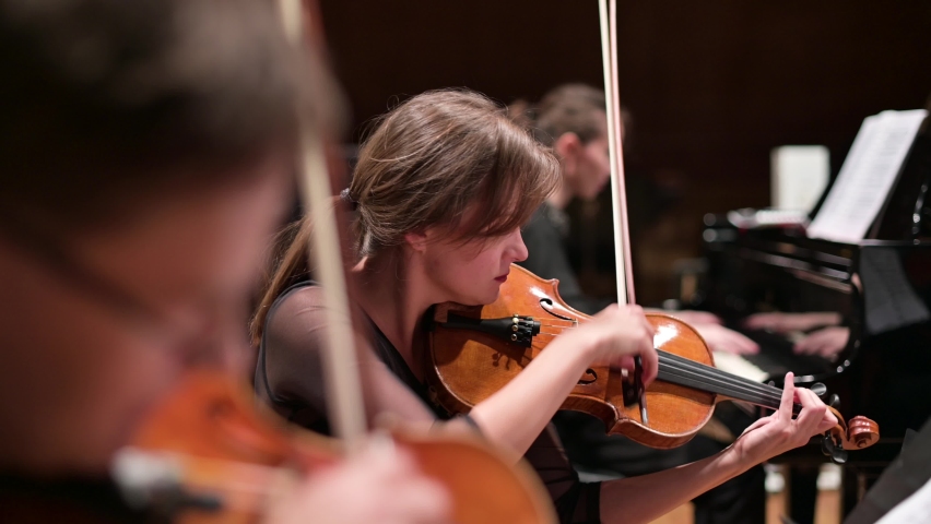 Focus on a young woman playing the violin with a string quartet and grand piano. Selective focus | Shutterstock HD Video #1062734212