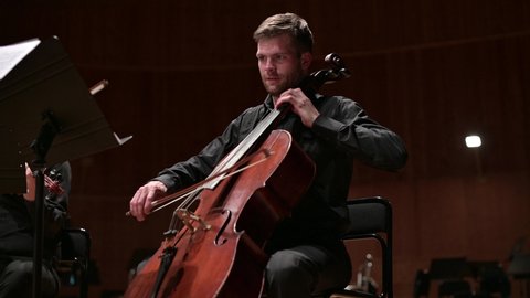 Young man in black clothes playing the cello, close up