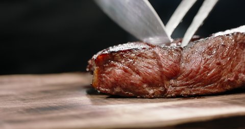 Close up shot of a juicy freshly grilled steak straight from the grid being cut with fork and knife on kitxhen table 0 food and drink 4k footage
