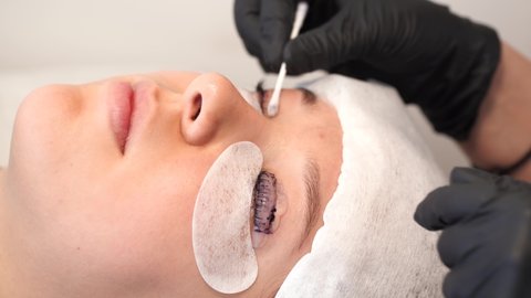 Closeup view 4k video of female face of young girl and professional cosmetologist doing modern spa cosmetic procedures of lashes lamination and dyeing.