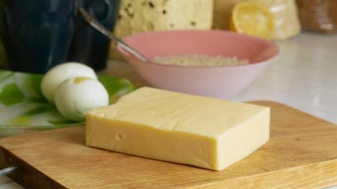 Cuts cheese on a wooden board.Cheese for breakfast in the home kitchen.Food preparation for proper nutrition.Low-calorie foods.Chicken eggs and oatmeal.Sharp kitchen knife.