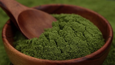 superfoods chlorella or spirulina powder in wooden bowl, rotating. green powder
